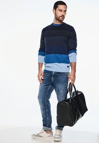 Marinblå och blårandig tröja med långa ärmar, matchad med ljusblå jeans och vita sneakers. Håller en svart läderväska.