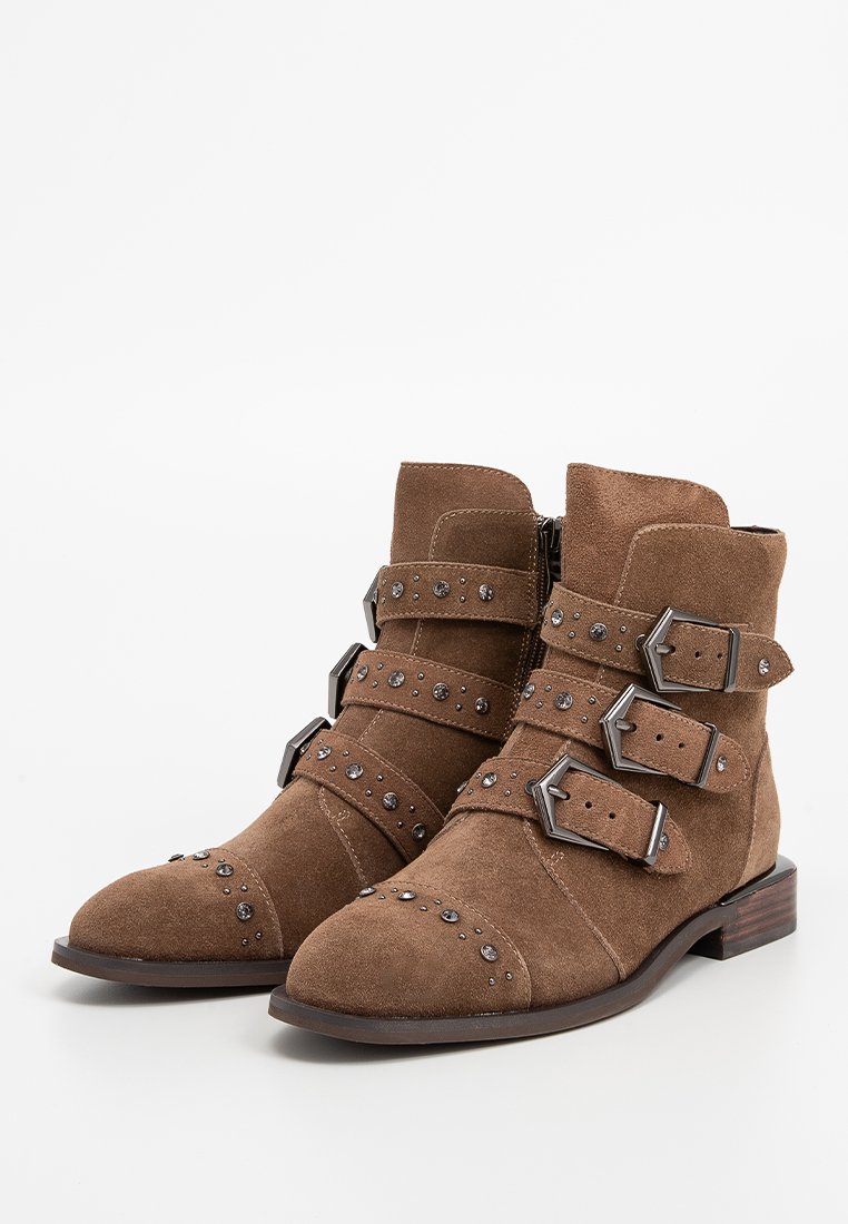 Stivaletti alla caviglia in suede marrone con tre ampie cinghie dotate di fibbie in argento e borchie, punta arrotondata, superficie texturizzata e tacco basso impilato.