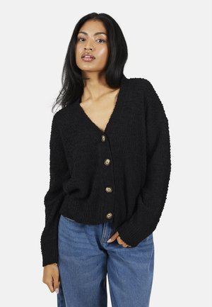 Zwarte gebreide cardigan met een V-hals, sluiting met knopen aan de voorkant en lange mouwen. Kenmerkt zich door gestructureerde stof en zes bruine knopen. G gedragen met hoge taille jeans.