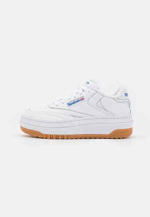 Baskets basses blanches Reebok avec logo bleu, détail Union Jack, devant à lacets, et semelle en caoutchouc gomme, vues de profil sur un fond blanc.
