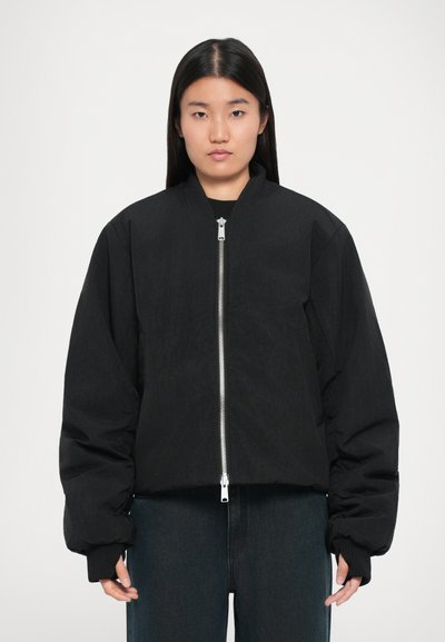 Chaqueta bomber negra con un corte relajado, cierre delantero de cremallera, puños acanalados y un acabado suave, ligeramente texturizado.