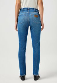 Tunna blå denimjeans med hög midja, bakfickor med ett dekorativt sömmönster och en läderlogotyp vid bakfickan.