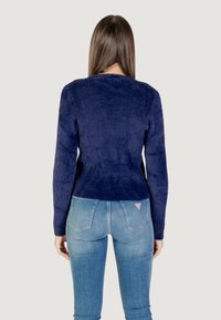 Maglione bleu navy, con texture, a maniche lunghe e scollatura rotonda, abbinato a jeans azzurri. Il maglione è aderente in vita.