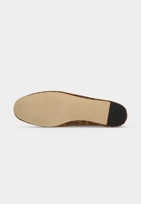 Semelle de chaussure plate avec dessous lisse beige, embout de talon noir et bord supérieur imprimé léopard visible sur fond blanc uni.
