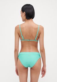 Un bikini de culoare verde mentă, cu textură canelată; bretele ajustabile. Dispune de un sutien cu tăietură modestă, cu o strălucire ușoară și un mic detaliu auriu.