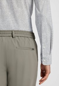 Spodnie elastyczne w jasnoszarym kolorze z tylną kieszenią, zestawione z wzorzystą białą koszulą z zapinanymi mankietami i teksturowanym materiałem.