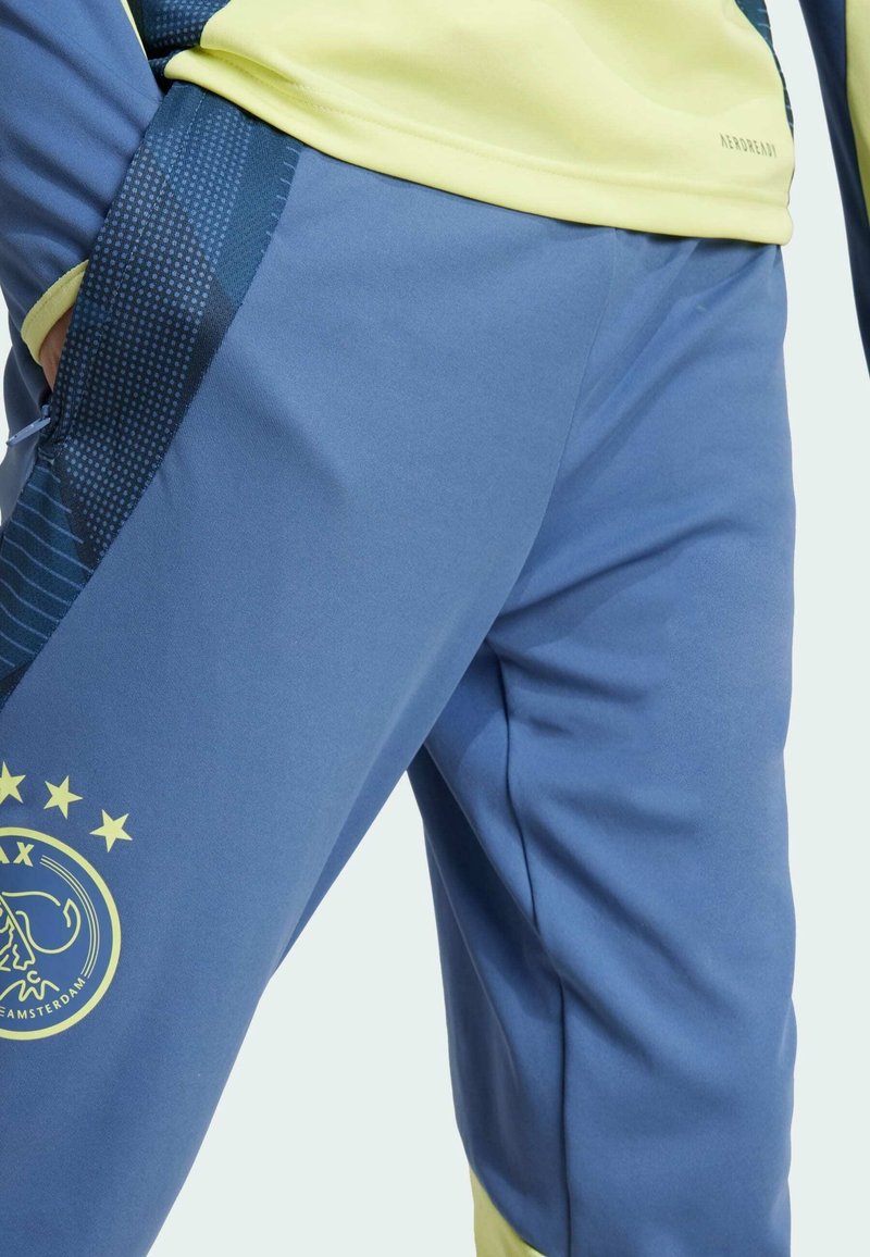 Pantalons de sport bleu avec une coupe slim, dotés d'un panneau latéral à motif bleu foncé et d'un accent jaune près de l'ourlet, avec un logo sur la cuisse.