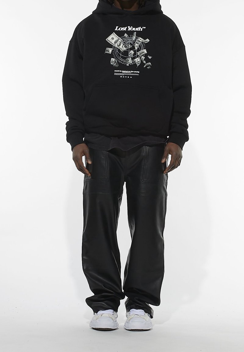 Svart hoodie med grafisk design som visar kontanter och en kompass. Kombinerad med svarta läderbyxor och vita sneakers, stående på en enkel bakgrund.