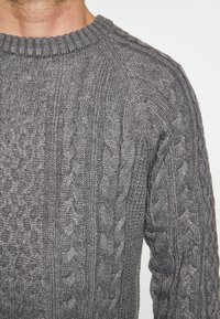 Pulover gri din tricotaj cu model cu zimți, de tip crew, cu guler rib și un model texturat ce prezintă cabluri alternative și mici bule.