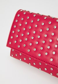 Pochette rose vif avec une surface texturée, ornée de clous en argent et d'accents ressemblant à des cristaux répartis de manière uniforme sur le devant.