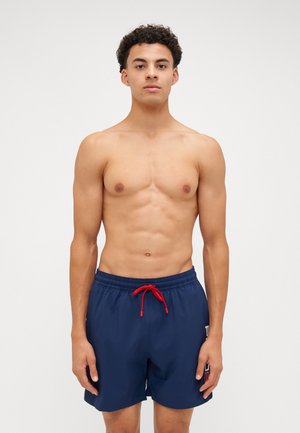 Navy blue swim trunks with elastic waistband, red drawstring, and side logo detail. Lightweight material, knee-length cut, smooth texture.