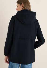Veste à capuche bleu marine avec une coupe décontractée, des manches longues et des poignets élastiques. Présente une fente au dos et un patch texturé sur l'épaule.
