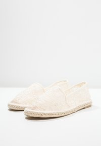 Baskets en dentelle couleur crème, dotées d'une semelle en jute tressé, d'un bout rond et d'un dessus en dentelle texturée avec des motifs floraux.