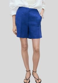 Modré ľanové šortky s prispôsobeným strihom, so bočnými vreckami a stredne vysokým pásom, doplnené čiernymi sandálmi na remienky.
