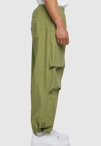 Olivenfargede, løstsittende cargo-bukser med sidelommer, elastisk midjebånd og justerbare cuffs, kombinert med hvite joggesko.