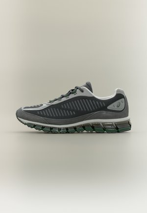 Šedá sportovní bota s texturovaným svrškem, zelenými akcenty a vícevrsvou podrážkou s vlnitým vzorem pro tlumení nárazů.