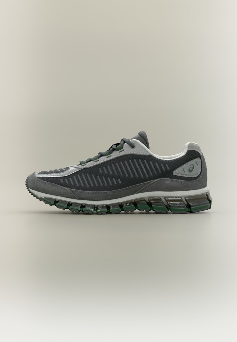 Szürke sportcipő, texturált felsőrésszel, zöld díszítésekkel és hullámos mintázatú, többrétegű talppal a jobb párnázás érdekében.