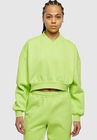 Felpa verde neon corta con scollatura a V e maniche ampie, abbinata a pantaloni elasticizzati in vita dello stesso colore, realizzati in un morbido tessuto testurizzato.