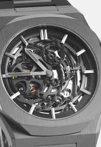 Montre squelette avec un boîtier et un bracelet en acier inoxydable gris. Présente des mécanismes internes complexes, de grands index horaires en argent et un design épuré.