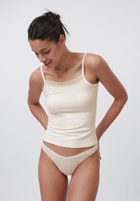 Beige geribbelde tanktop met kantafwerking bij de halslijn, gecombineerd met bijpassende beige onderbroekjes met kantafwerking. Beide artikelen hebben een aansluitend ontwerp.