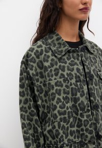 Leopard-patterned jacket in muted green tones, featuring a collared neck, button closure, and a chest pocket with a textured finish.