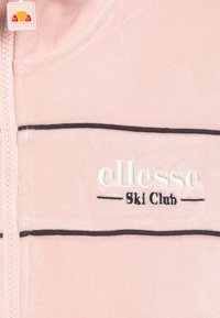 Giacca zip-up in velour rosa con strisce nere e logo ricamato "ellesse Ski Club". Texture morbida con un design sportivo.