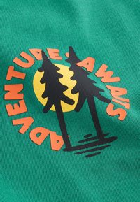 Tessuto verde con superficie strutturata presenta un design grafico con due alberi neri e un sole arancione, affiancato dal testo "L'AVVENTURA TI ASPETTA."