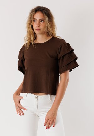 Top in cotone marrone con maniche corte a balze stratificate, scollatura rotonda e design corto, abbinato a jeans bianchi a vestibilità aderente.