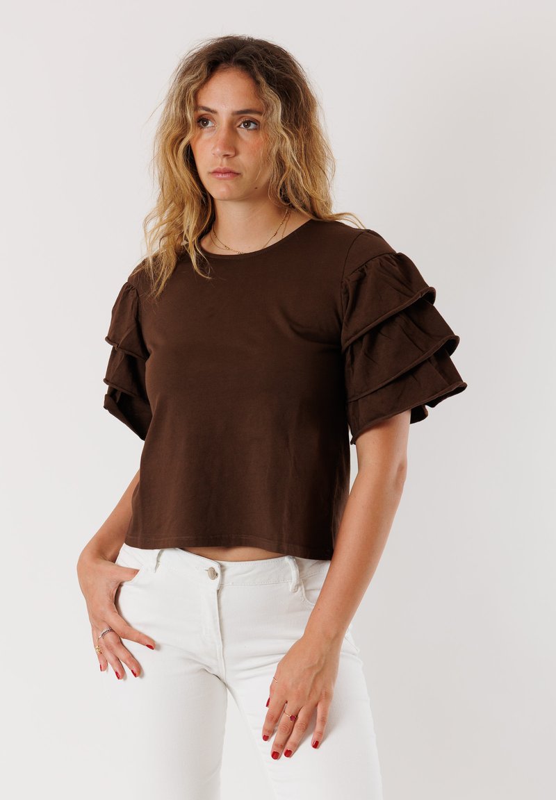 Top in cotone marrone con maniche corte a balze stratificate, scollatura rotonda e design corto, abbinato a jeans bianchi a vestibilità aderente.