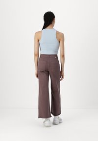 Débardeur côtelé bleu clair, pantalon large marron avec des ourlets effilochés, et baskets blanches, vu de dos.