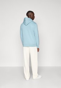 Φωτεινό γαλάζιο φούτερ με κουκούλα και άνετη εφαρμογή, συνδυασμένο με χαλαρά κρεμ παντελόνια και λευκά αθλητικά παπούτσια. Απλός σχεδιασμός, με ελάχιστες λεπτομέρειες.