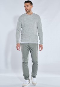 Grau strukturierter Strickpullover mit Rundhalsausschnitt, kombiniert mit schlank geschnittenen hellgrünen Hosen und beigen Sportschuhen. Schlichtes Design und Passform.