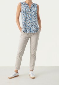 Květinová bezrukávová blůza s modro-bílými vzory; lehká tkanina. V kombinaci se světlými slim-fit kalhotami a bílými teniskami.