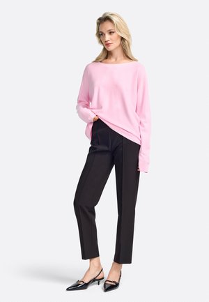 Maglione rosa chiaro con maniche lunghe abbinato a pantaloni neri sartoriali e scarpe slingback nere con punta affusolata. Tessuto liscio, vestibilità comoda.