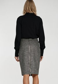 Czarna bluzka z długim rękawem i szara dopasowana spódnica ołówkowa z teksturowanej tkaniny i centralnym zapięciem na zamek z tyłu.