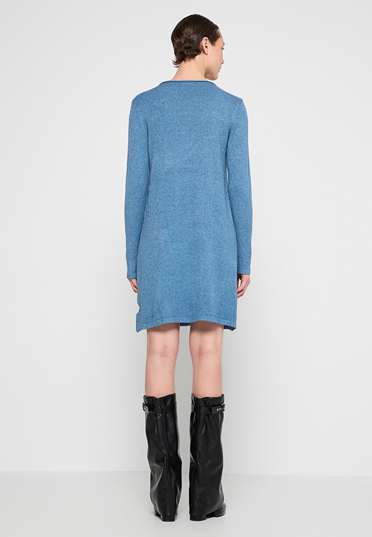 Robe en tricot bleu à manches longues, silhouette droite et encolure arrondie. Portée avec de longues bottes en cuir noir.