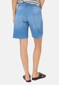 Shorts en denim bleu clair, avec une taille mi-haute, deux poches arrière et un ourlet roulé, accompagnés de sandals noires à enfiler.