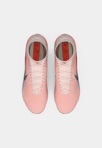 Gaiši rozā sporta apavi ar teksturētu rakstu, melnu logo, zilām akcentiem un baltām šņorēm. Iezīmējas ar mīkstu iekšzoli un noapaļotu pirkstu daļu.