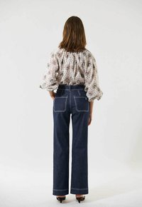 Bluse med blomsterprint, letvægtsmateriale og pufærmer, parret med mørkeblå, vidde jeans med hvid syning og baglommer.