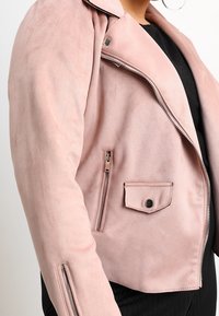 Różowa kurtka motocyklowa z imitacji zamszu z skośnymi klapami, kieszeniami na zamek i kieszenią z patką na zatrzask. Gładka tekstura i dopasowany krój.