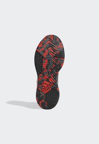 Suela de zapatilla deportiva negra y roja con patrones texturizados, que presenta surcos distintivos y un logotipo prominente en el talón.