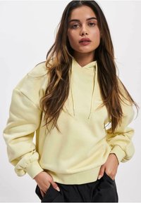 Sweatshirt à capuche jaune avec une coupe décontractée, des poignets côtelés et un tissu texturé. Comprend des cordons de serrage et une poche kangourou à l'avant.