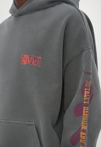 Sweat à capuche gris avec un logo "KSUBI" imprimé sur la poitrine et des graphismes colorés le long de la manche. Fabriqué en tissu doux et texturé.