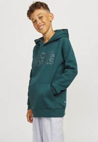 Felpa verde realizzata in tessuto morbido, dotata di tasca a canguro e di un grande logo discreto. Il design include un cappuccio con cordino e polsini a costine.