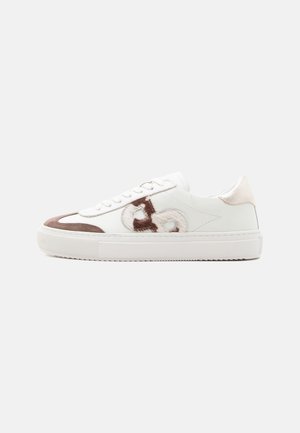 White low-top sneaker with brown suede accents, white laces, and a brown and beige embroidered logo on the side against a plain background.