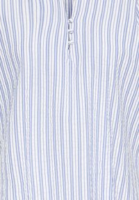 Tissu de chemise à rayures verticales bleues et blanches avec trois petits boutons recouverts du même tissu près du centre.