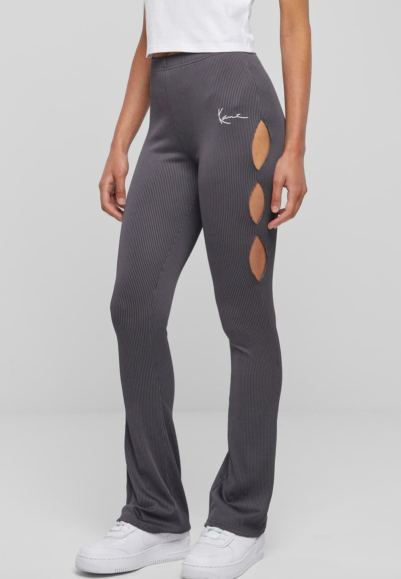 Pelēkas ribotas leggingas ar izgriezumiem sānos, ar nelielu baltu logotipu gurnā un pieguļošu dizainu.