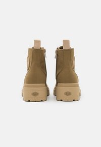 Botas de tobillo de lona color beige con cierre lateral, parte superior texturizada y suela de goma con acentos de logo. Diseño ligero y resistente.