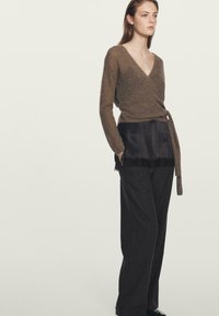 Maglione marrone avvolgente con scollo a V e cintura in vita, abbinato a pantaloni larghi a righe. Tessuto morbido con dettagli in pizzo.