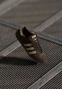 Sneaker in suede marrone con tre strisce dorate, suola in gomma e punta cucita. Presenta chiusura con lacci e logo del marchio sulla linguetta.